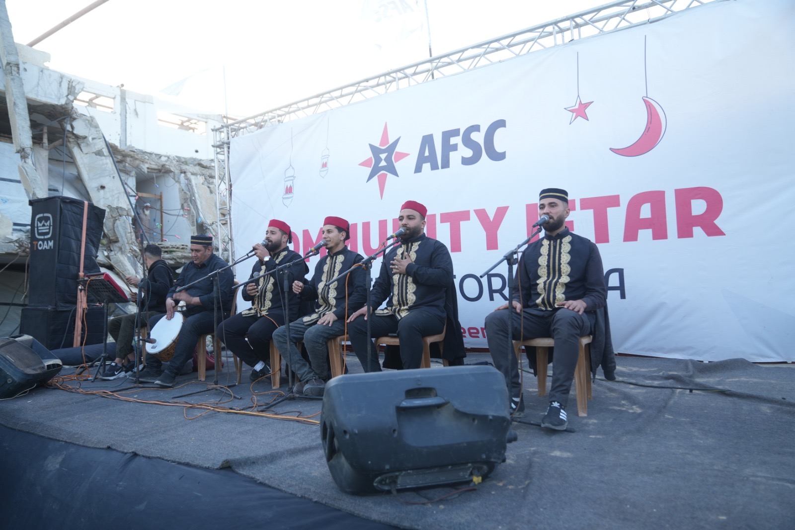 Several men sitting in chairs on a stage perform music