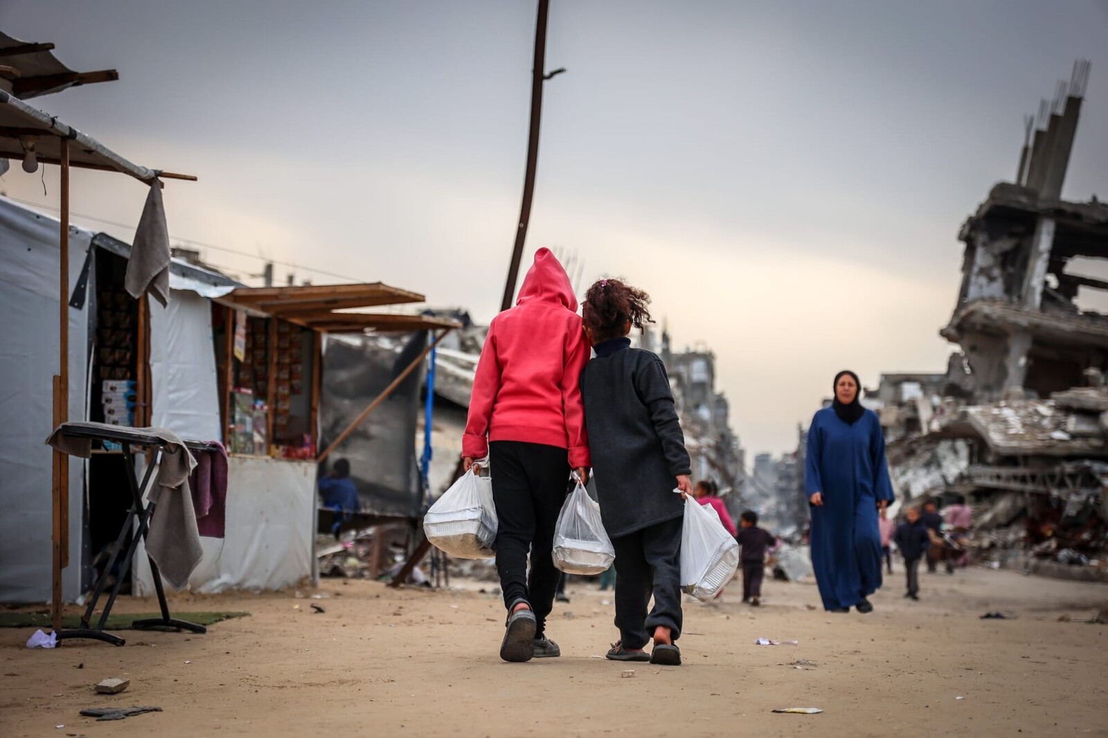 Two children walk side by side while carrying hot meals from AFSC.