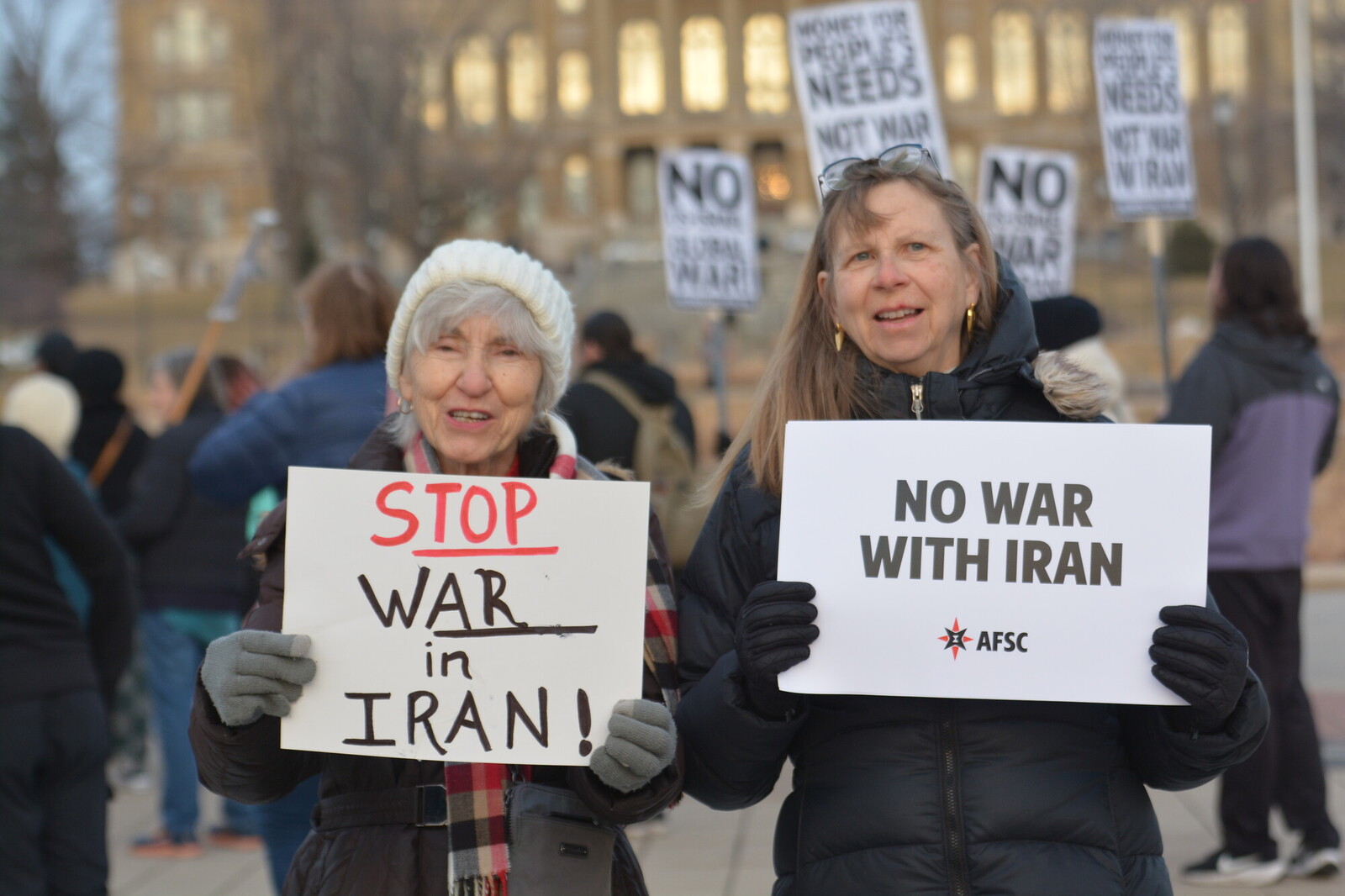 2 people holding signs opposing war with Iran 