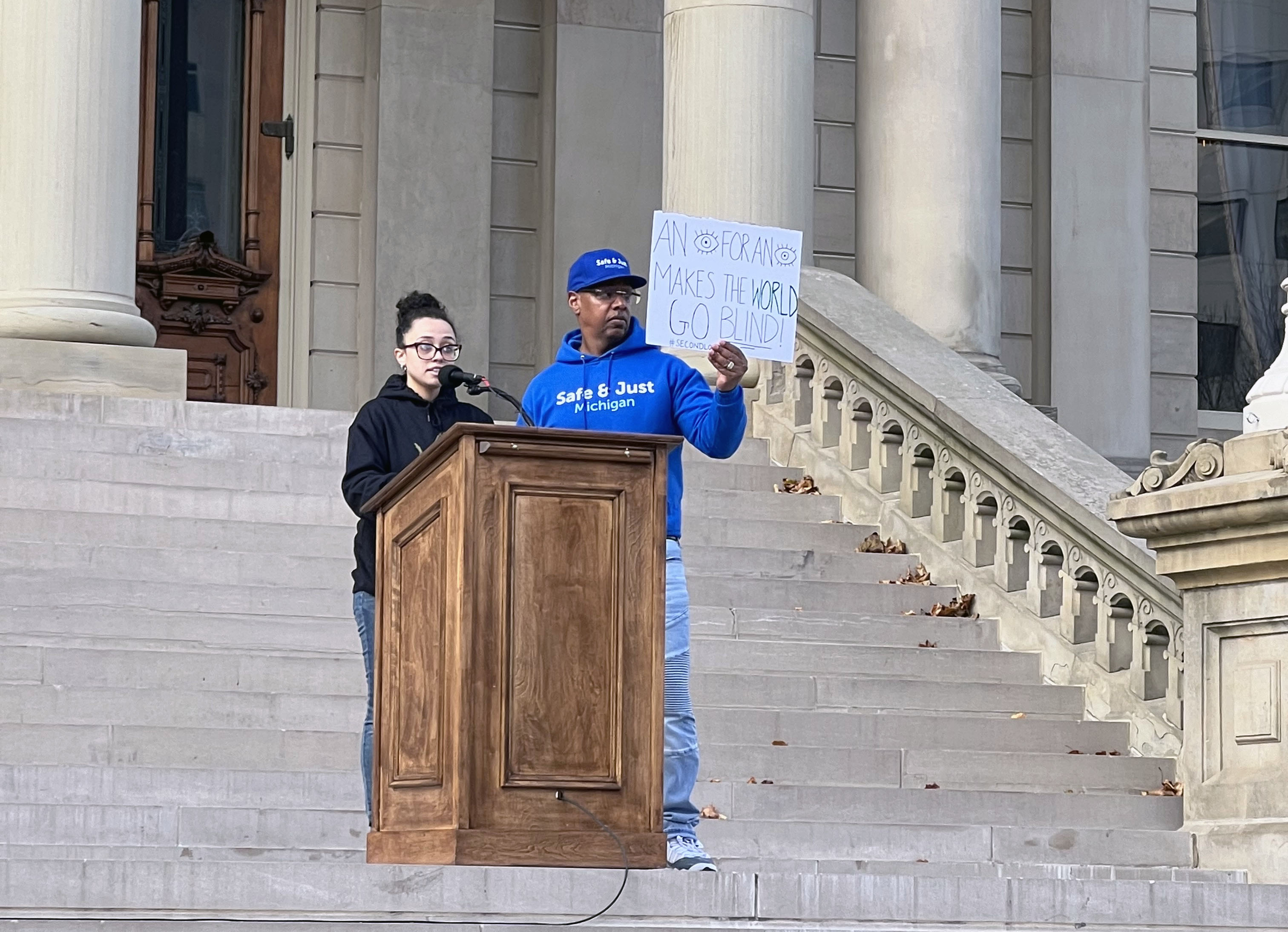 photo of two people at podium in front of a government building