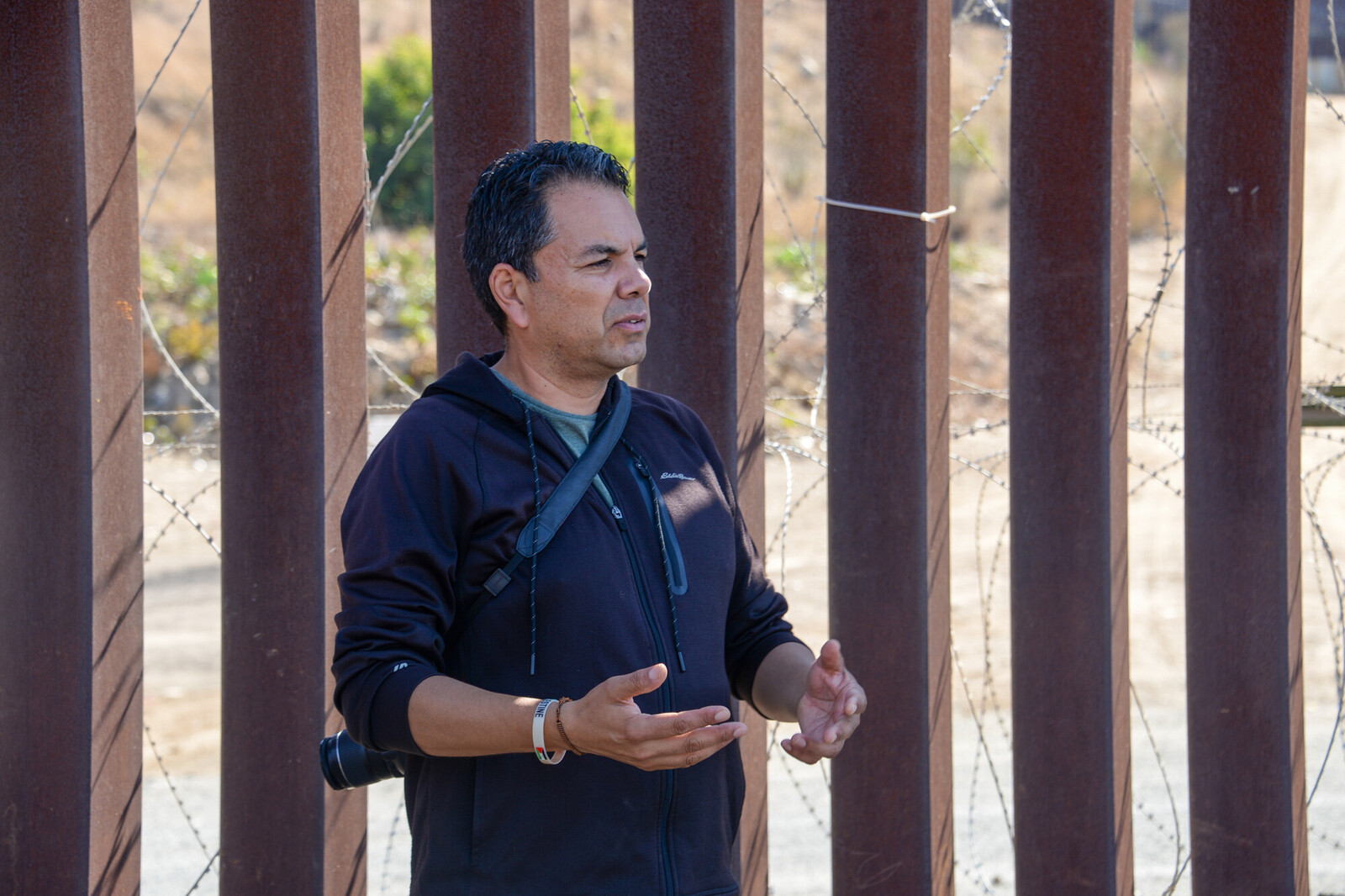 photo of pedro rios in front of a rusted border wall
