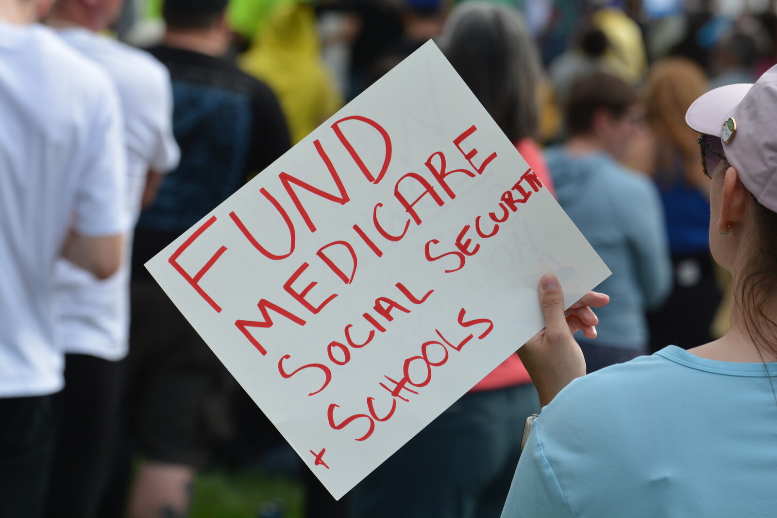 photo of someone holding sign that reads fund medicare, social security and schools