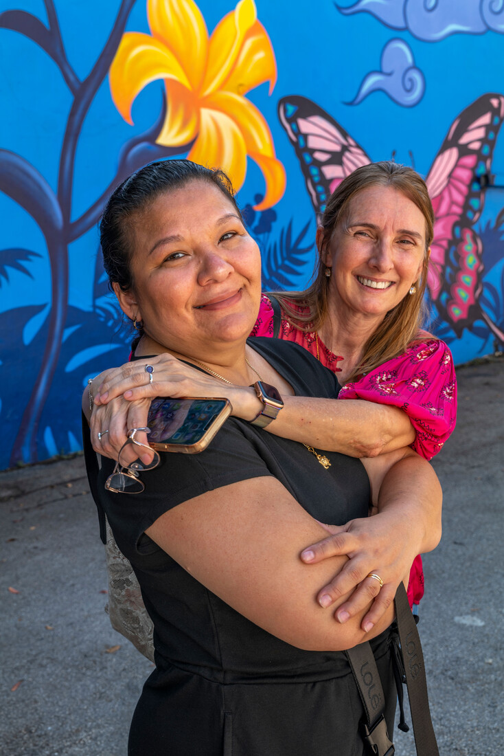 Photo of two people hugging each other there is a butterfly mural in the background