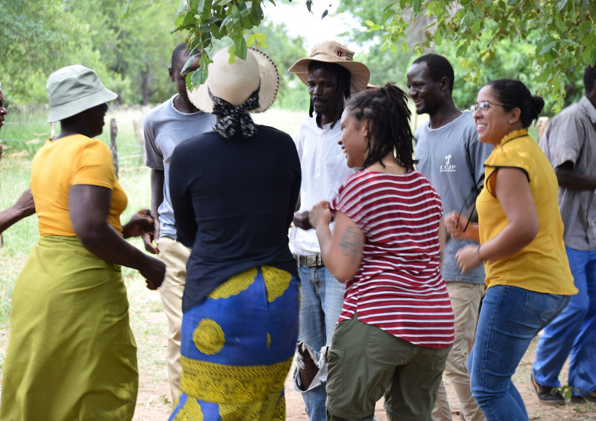people dancing in a circle lush greenery behind theyrm 