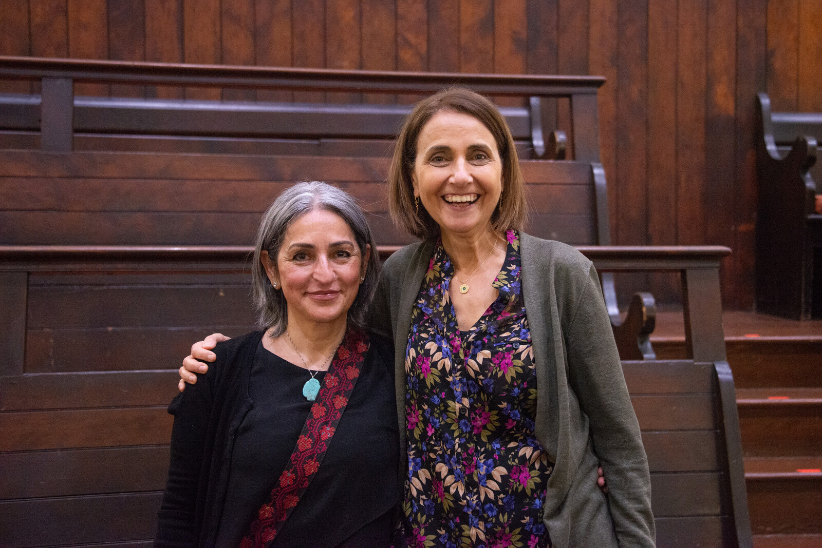 Joyce standing next to corporation memeber in a friends meeting house. Dark wood behind them