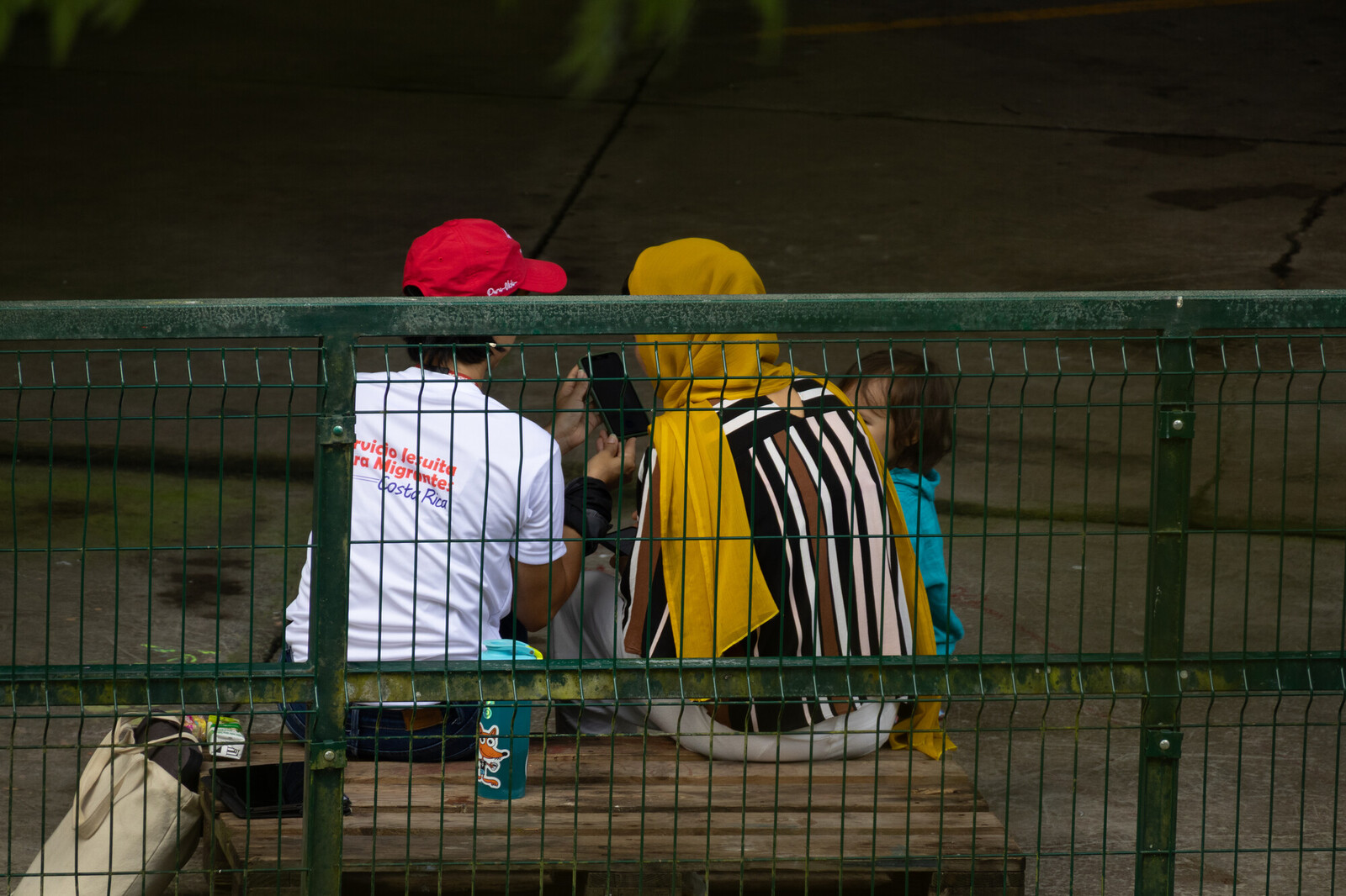 two people sitting behind a green fence in detention center