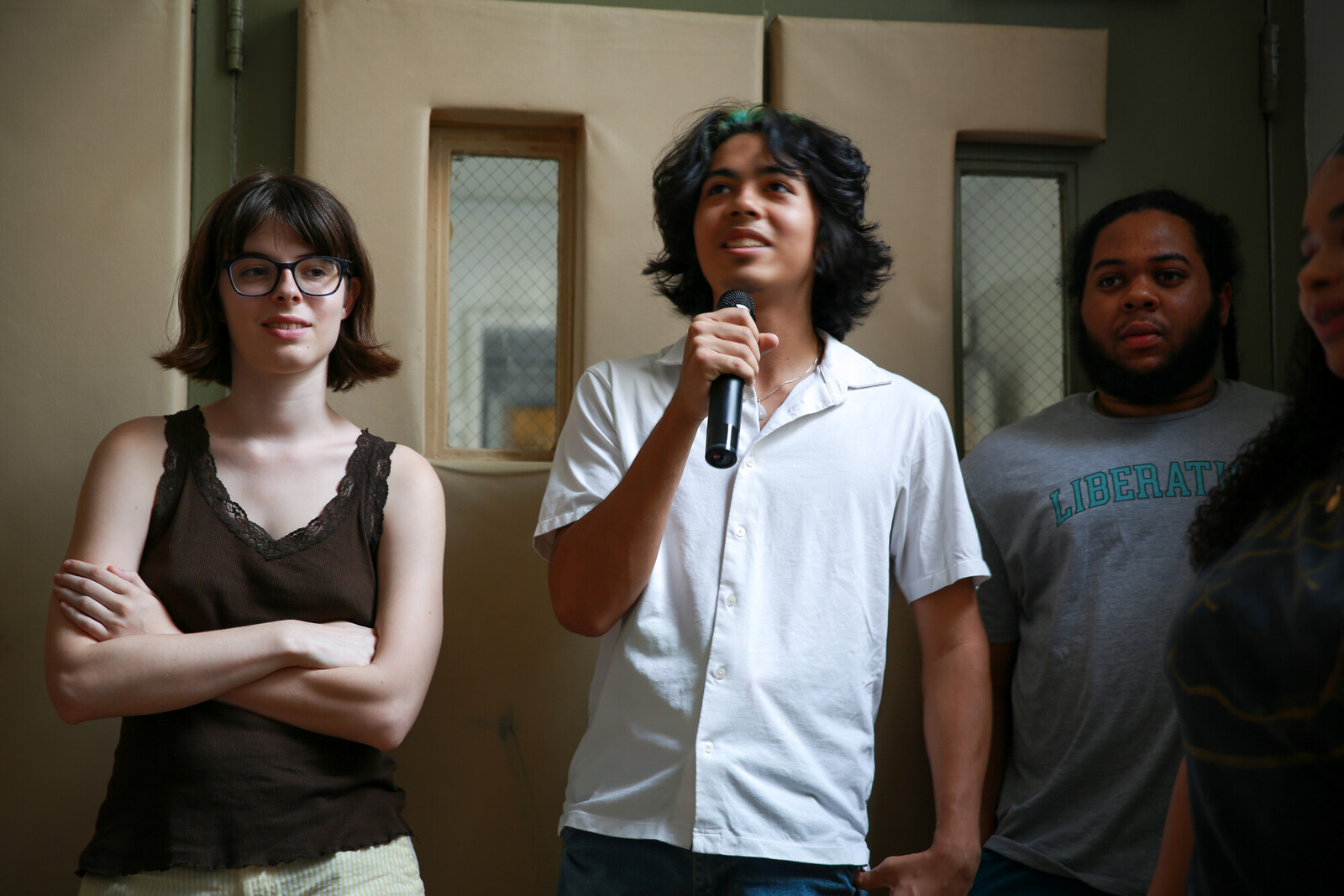 three young people in a room, the middle person is holding up a microphone looking up towards the ceiling.