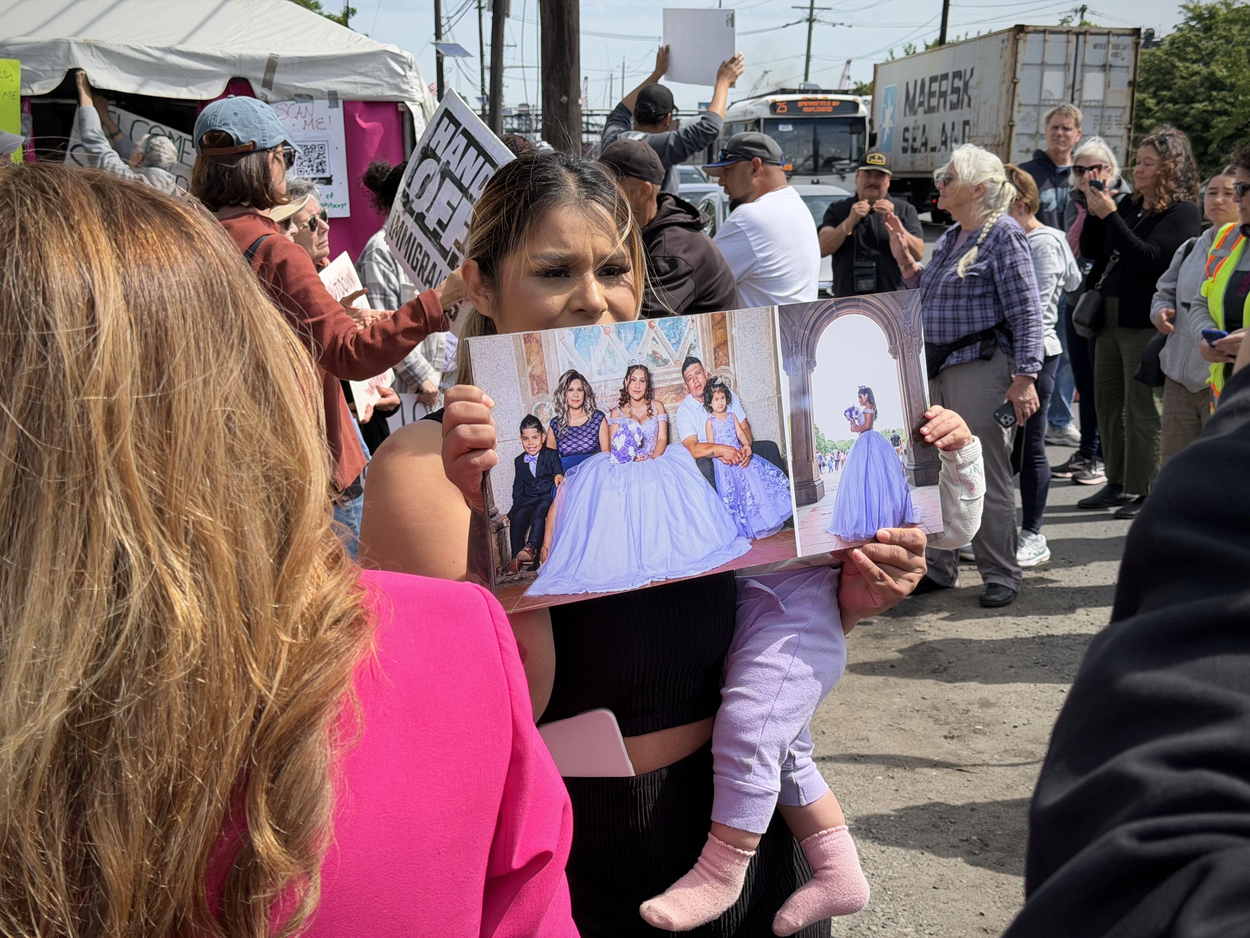 A woman holds up a photo of a family and a child in her arms