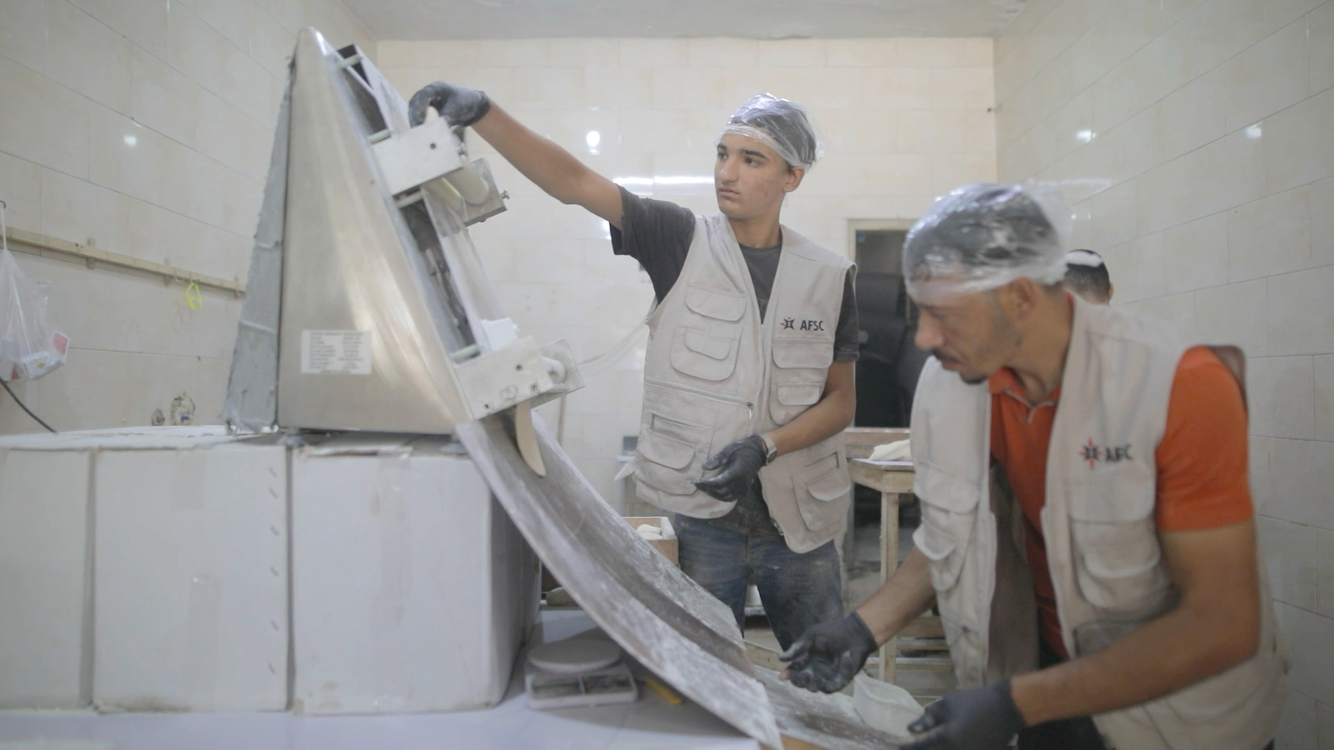 Two people feed dough through a bread maker