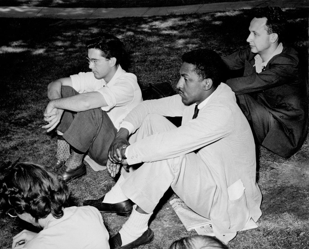 Bayard Rustin (center) sits with 2 others on the grass
