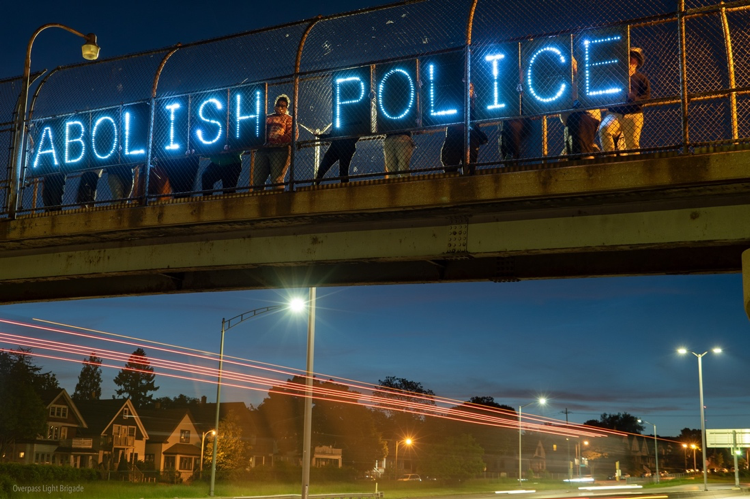 A message made out of light boards that reads "Abolish Police" is hung over a highway overpass.